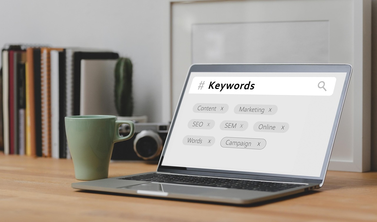 laptop screen displaying a search bar with the word 'keywords,' with a camera and books behind it