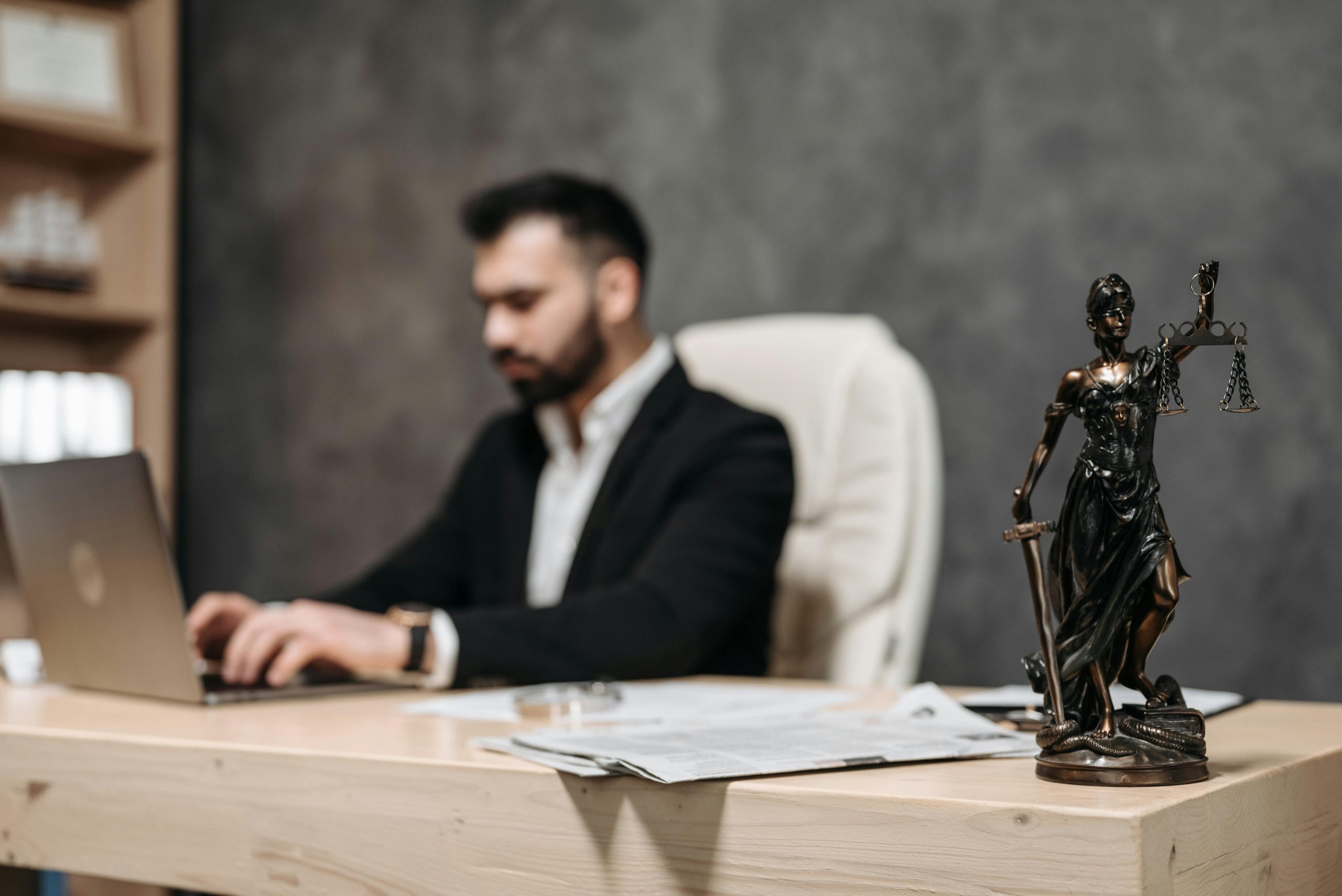 lawyer working on a laptop with a Lady Justice figurine next to him